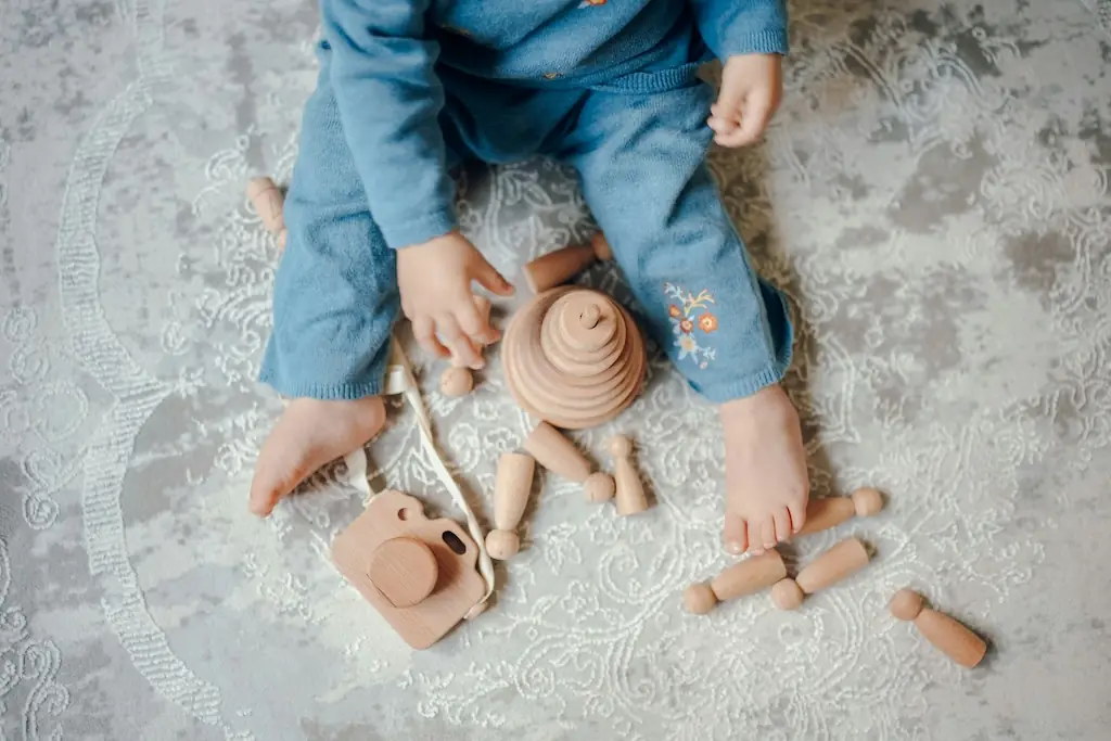 Overhead view of a child in blue playing with a wooden toy camera, peg dolls and a stacking cone